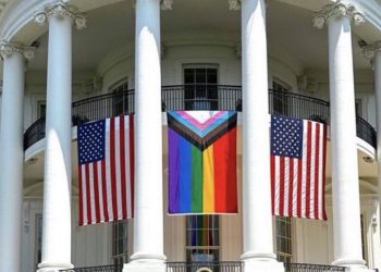 A Pride Progress flag hangs on the White House between two American flags.
