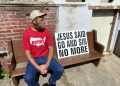 Damon Atkins sits on a bench outside his home in central Reading. A sign sits besides him with the words, "Jesus Said Go and Sin No More."